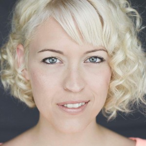 Head and shoulders photo of Lindsay Goldapp, Artistic Director of Stomping Ground Comedy. Lindsay has short curly blonde hair and 