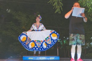 Woman from Alegre Ballet Folkorico wearing Mexican regalia and man reading program standing on stage