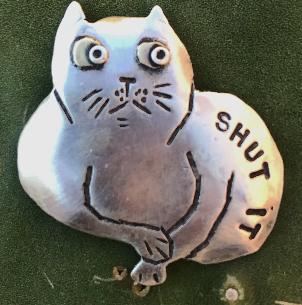 jewelry pin of a cat with "shut it" written on it