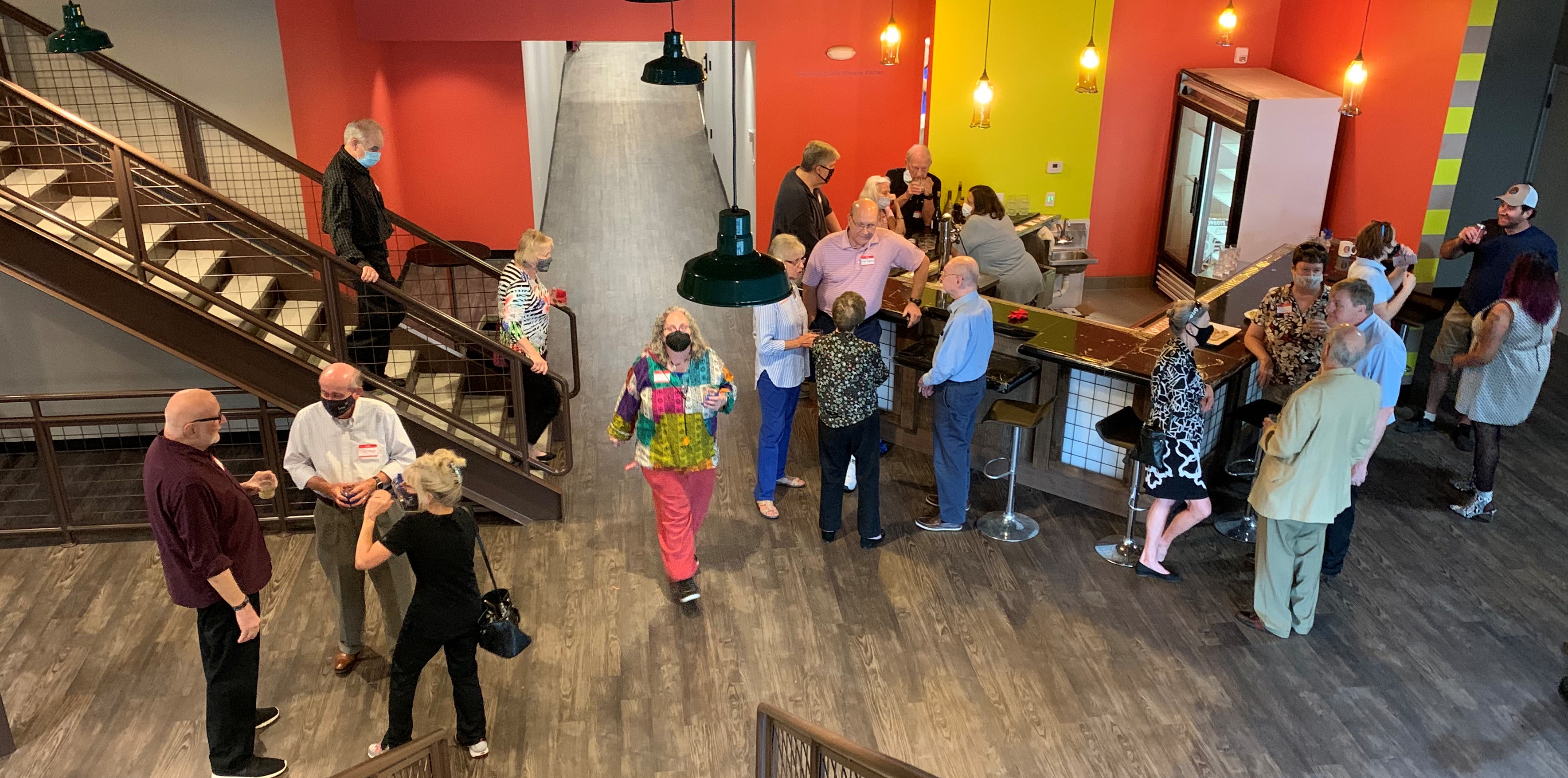 People stand around Stage West's new lobby, which has orange and yellow walls and a small bar area.
